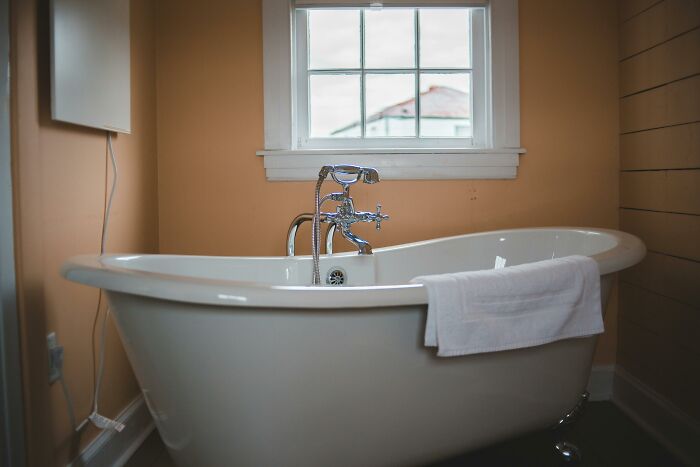 Bathtub with towel in a cozy bathroom, natural light from window highlighting clean design amid wooden and orange walls.