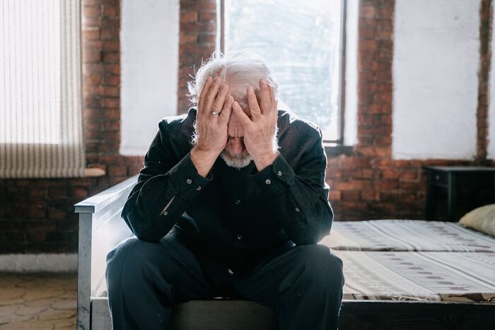 Elderly man sitting on a bed, head in hands, contemplating secrets about jobs.