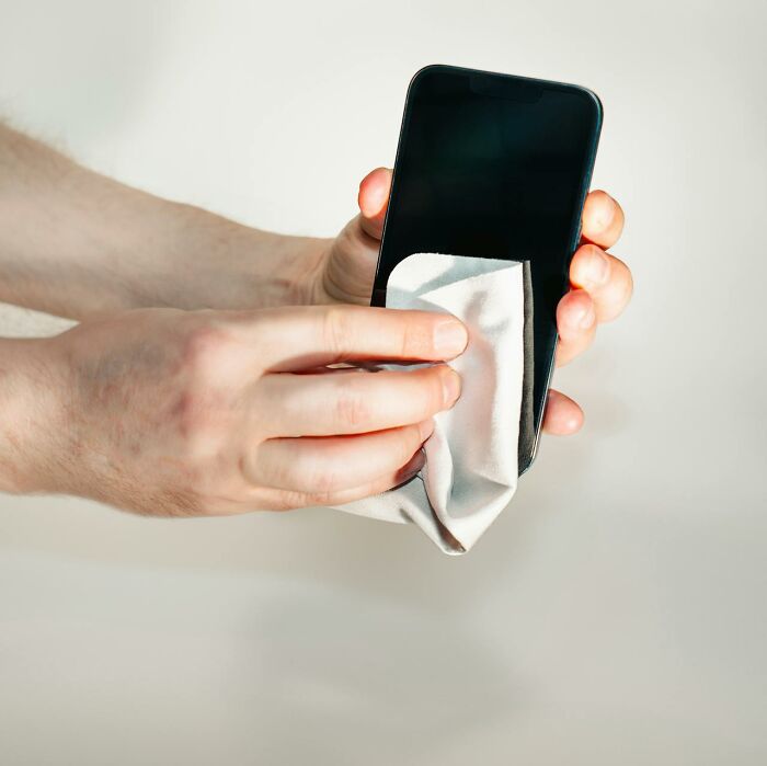 Cleaning a smartphone with a cloth to maintain hygiene habits.