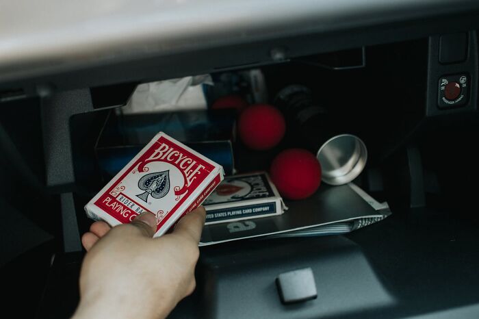 Hand reaching into a car glove compartment with red balls and a deck of Bicycle playing cards, symbolizing dating an idiot.