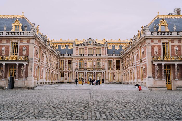 Historic Versailles facade with golden details, courtyard view; significant cultural influence.