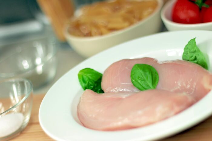 Raw chicken breasts on a plate with basil leaves, blurred background with kitchen ingredients, highlighting quick job loss theme.