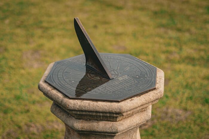 A sundial on a stone pedestal casting a shadow on a grassy background.