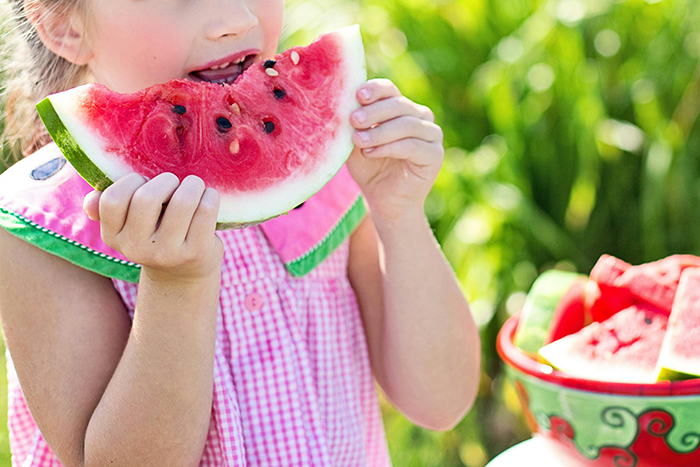 Child enjoying a slice of watermelon outdoors, illustrating food preferences and dietary habits.