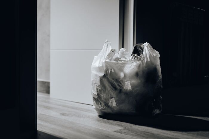 Plastic bag reused as trash bin in a dimly lit room, illustrating a frugal habit developed from being poor.