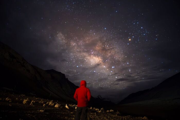 A person in a red jacket gazing at a starry night sky, highlighting a moment of realization under the Milky Way.