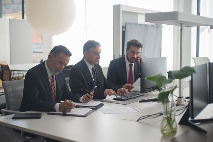 Three businessmen in suits working at a modern office desk, representing job secrets in a corporate setting.