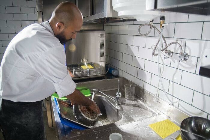 Person washing dishes in an industrial kitchen, illustrating one of the worst jobs experienced by 32 people.