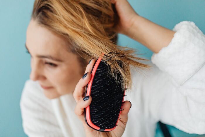 A woman brushing her hair with a red and black brush, emphasizing hygiene habits.