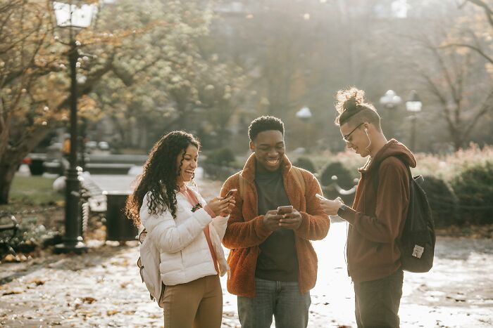 Friends enjoying peace and quiet while using phones in a park during a sunny day.