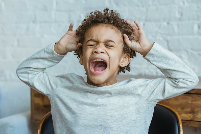 Rich kid expressing frustration, sitting in a chair with a white shirt against a brick wall background.