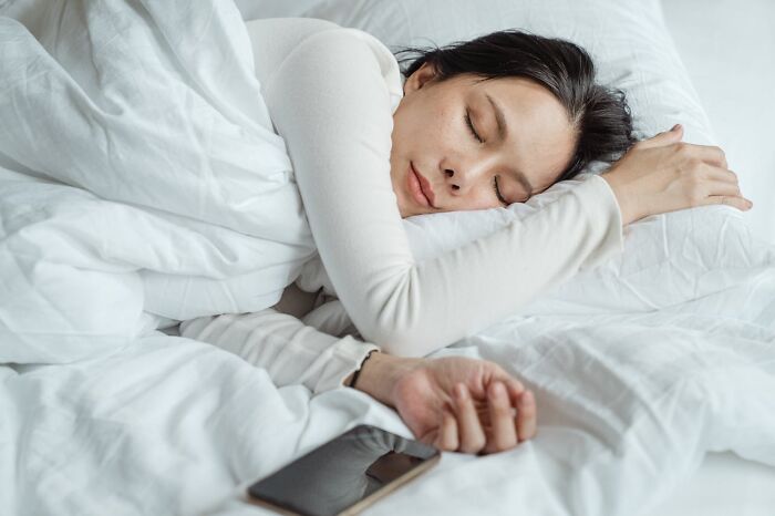 Person sleeping peacefully in bed with a smartphone nearby, symbolizing rest and the importance of job secrets.