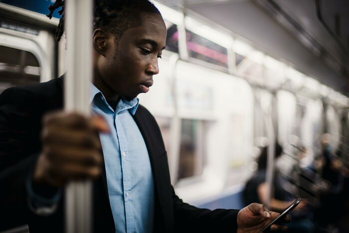 Person in a subway car, wearing a blue shirt and dark jacket, focused on their phone, representing secret judgment scenarios.