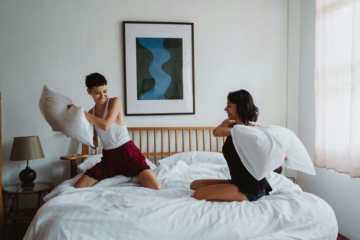 Two people having a pillow fight on a bed, smiling and enjoying a moment together.