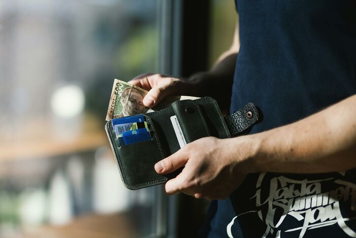 Person holding a wallet with cash and cards, illustrating things people secretly judge others for.