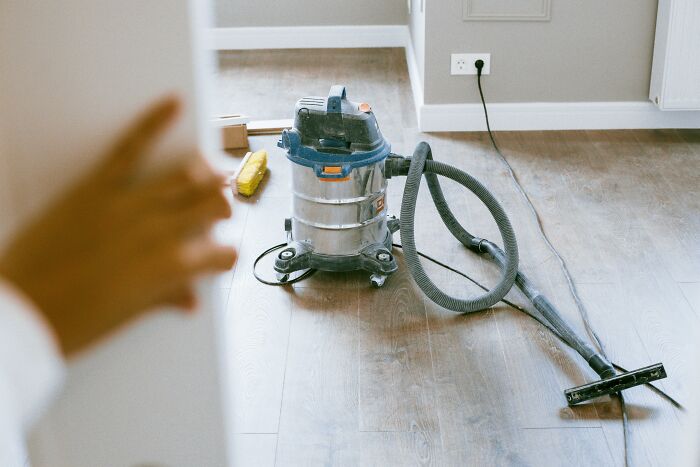 Vacuum cleaner on wooden floor, part of the WomenInMaleFields trend highlighting nontraditional roles.