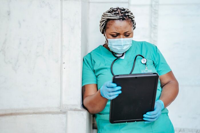 Healthcare worker in scrubs, mask, and gloves, looking at a tablet, revealing job secrets.