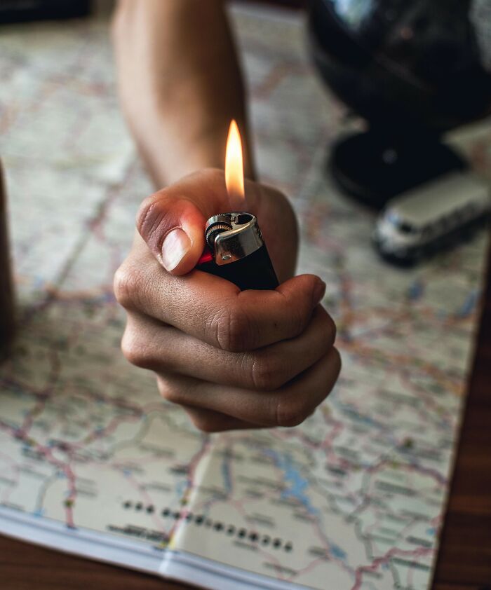 Hand holding a lit lighter over a detailed map, representing travel and exploration; a rare everyday fact.