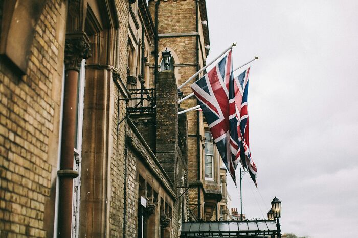 Union Jack flags on a historic building influencing history, cloudy sky in background.