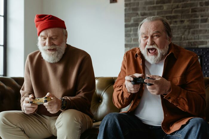 Two elderly men joyfully playing video games on a couch, highlighting a contrast to picking daffodils as a worst job experience.