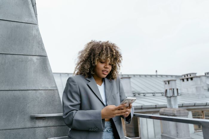 Woman in a gray blazer uses a smartphone on a rooftop, representing the WomenInMaleFields trend.