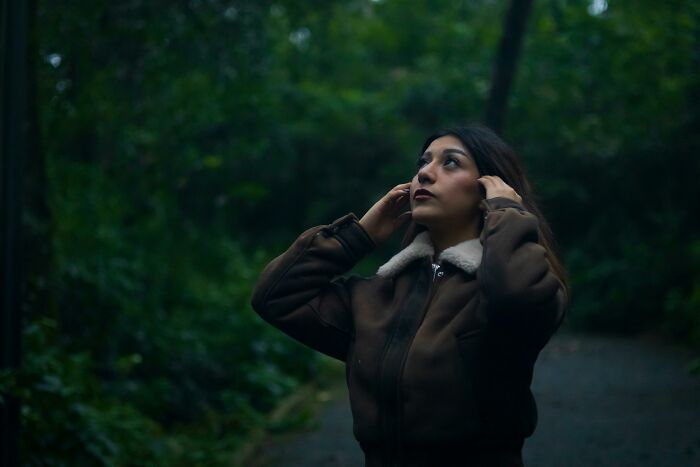 Woman enjoying peace and quiet in a serene, forested path, wearing a brown jacket with fur collar.