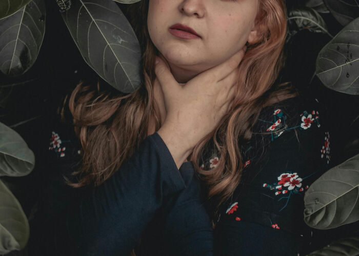 Woman with a floral top and blonde hair, hands on neck, surrounded by dark leaves, representing dating an idiot moment.