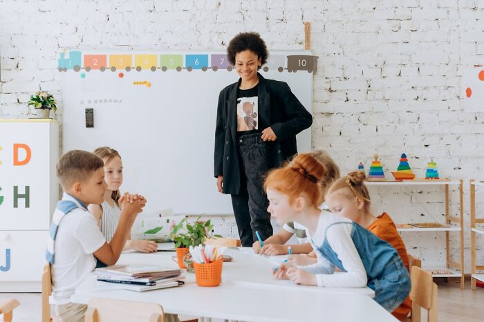 Teacher engaging with students at a classroom table, illustrating a 'fun' job that may be less enjoyable than imagined.