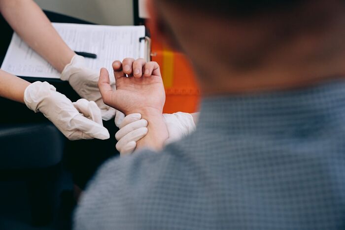 Doctor measuring pulse, emphasizing exercise importance, while wearing gloves and holding a patient's wrist.