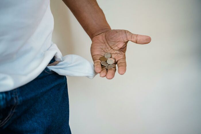 A person holding coins in one hand, with an empty jeans pocket inside out.