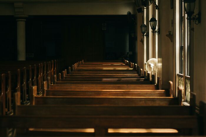 Empty church pews illuminated by soft window light, reflecting solitude and contemplation about professions.