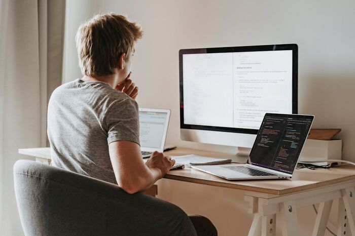 Person working on computer screens at home office, contemplating project, representing sudden job loss scenario.