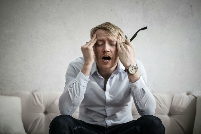 A frustrated person in a white shirt on a couch, expressing stress or disappointment.