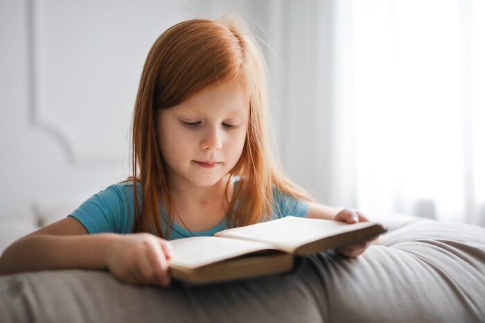 A young girl with red hair reads a book, discovering hidden job secrets in a cozy home setting.