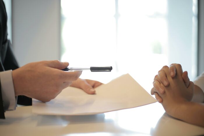 Person handing over documents and a pen in an office setting, symbolizing discussion about worst jobs like picking daffodils.