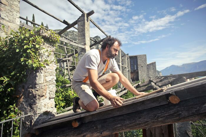 Man working on rustic wooden structure under a clear sky, illustrating tough job challenges.