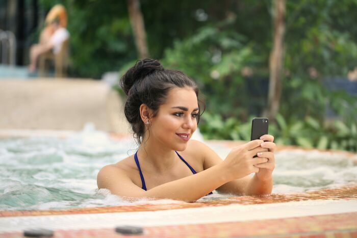 A woman in a pool taking a selfie with her phone, capturing the essence of WomenInMaleFields trend.