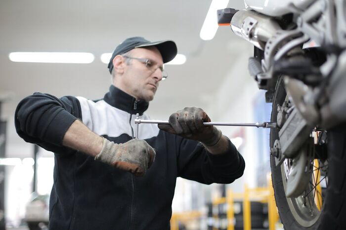 Mechanic in a workshop using a wrench on a motorcycle, sharing job secrets not known to the public.