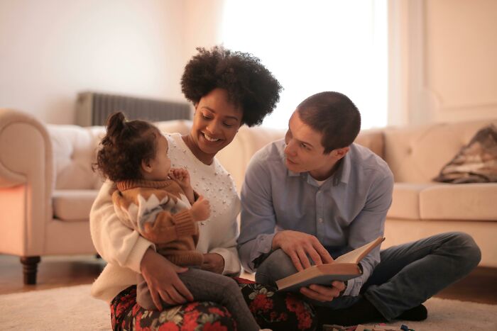 Family enjoying peace and quiet at home, sitting together on the floor with a book in a cozy living room setting.