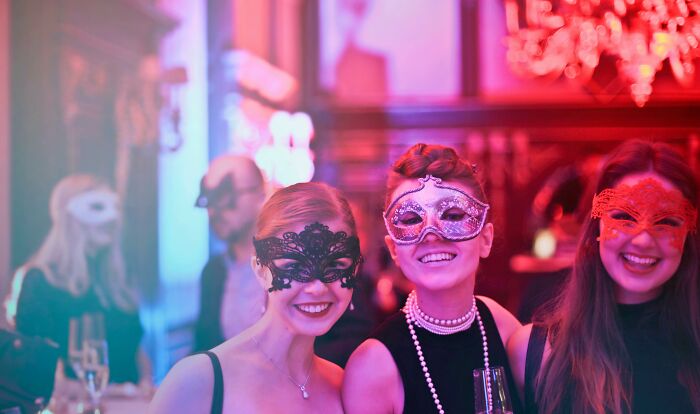 Masked party attendees smiling and holding drinks, suggesting people sharing secrets at an event.