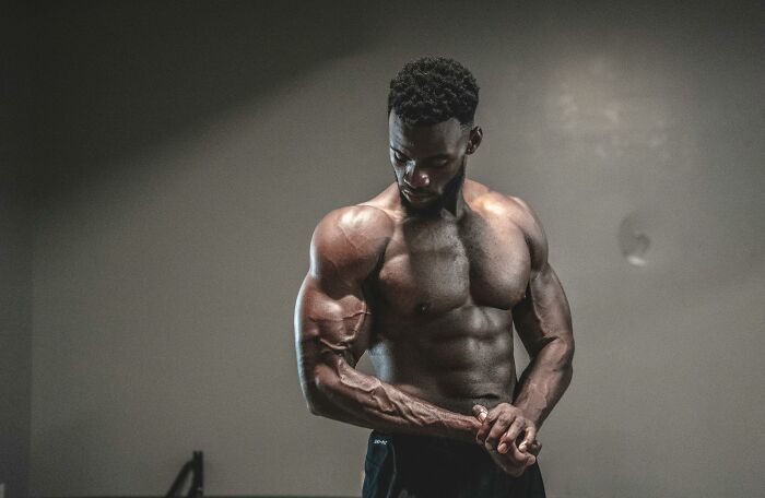 Man showcasing muscular physique in a gym setting, exemplifying fitness and strength.