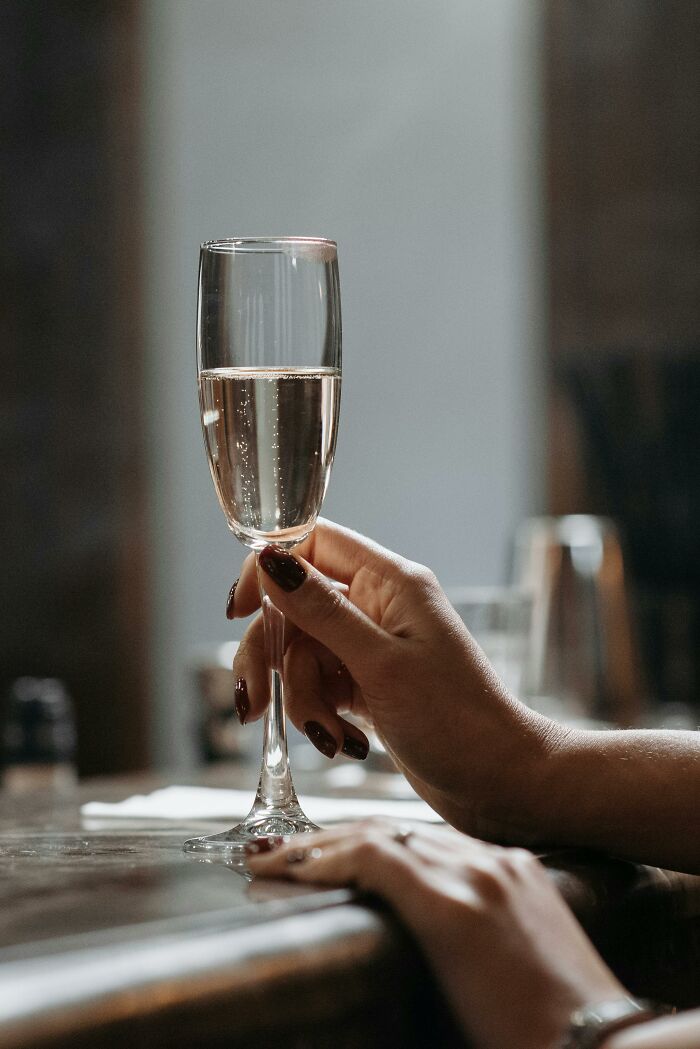 A hand holding a champagne flute at a bar, reflecting anticipation.