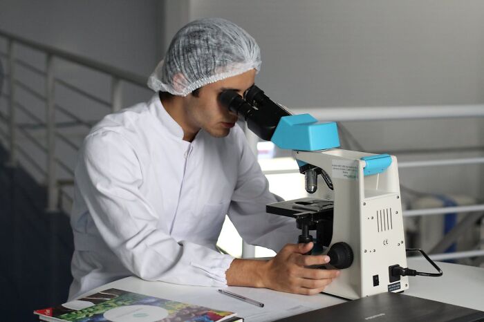 Scientist in lab coat using microscope, revealing job secrets through research analysis.