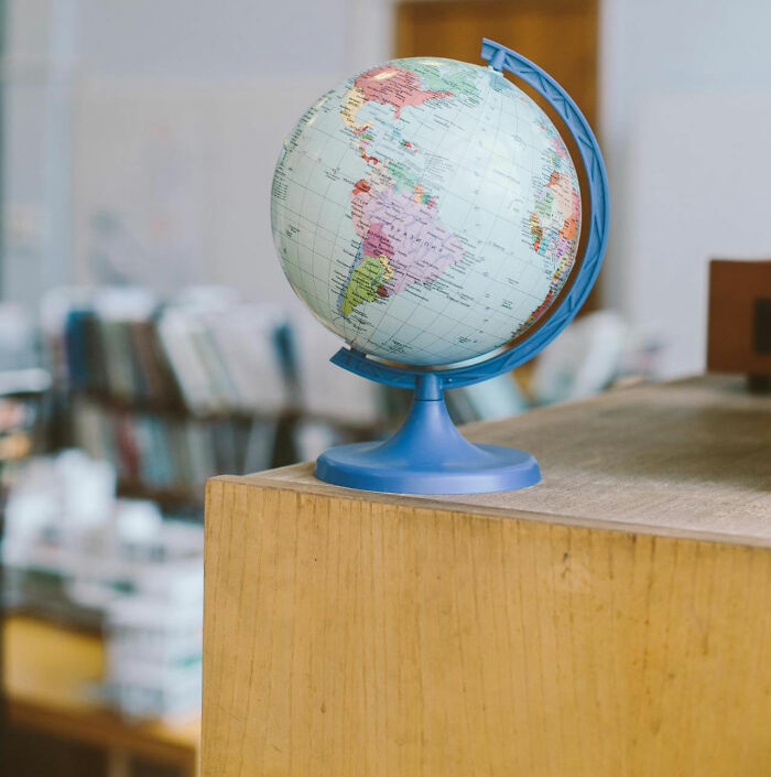 A globe on a wooden table in a library setting, representing the moment realized.