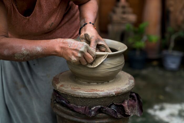 Person shaping clay on a pottery wheel, hands covered in mud, illustrating a job less fun than imagined.