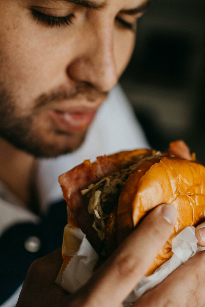 Man realizing he's dating an idiot while eating a messy burger, looking disappointed and thoughtful.