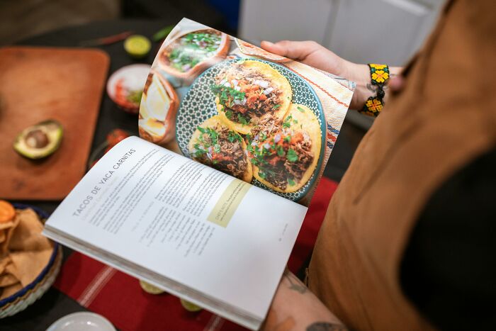 Person holding a cookbook, showing a frugal home hack for making delicious tacos with affordable ingredients.