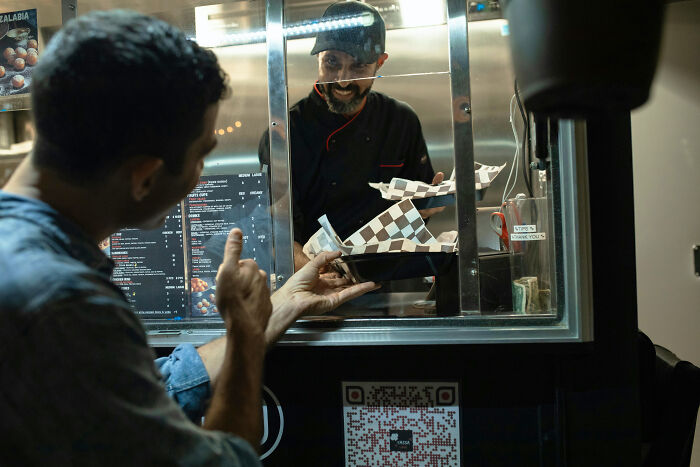 Traveler in a cringeworthy situation ordering food from a street vendor through a small kiosk window.