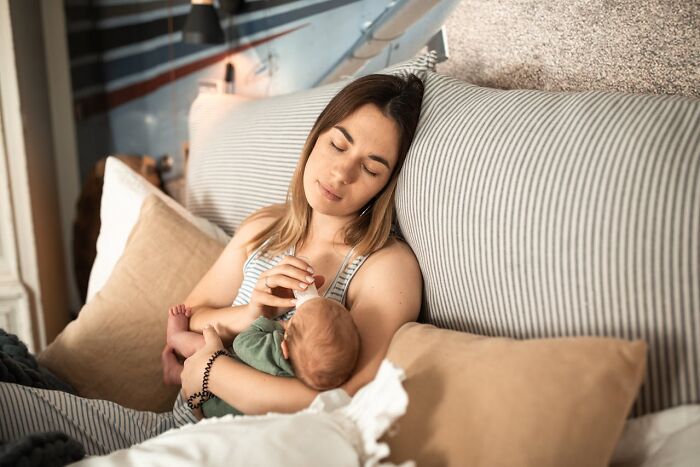 Woman resting with a baby on a striped couch, embodying peaceful moments during a busy day.