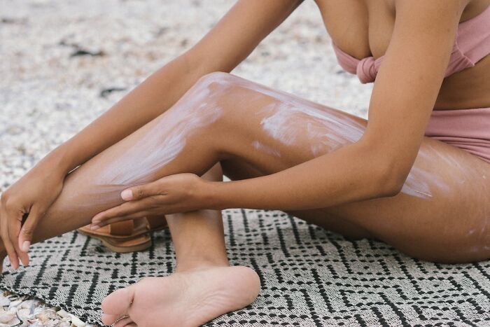 Person applying lotion on their leg, sitting on a patterned mat, highlighting exercise readiness and self-care.